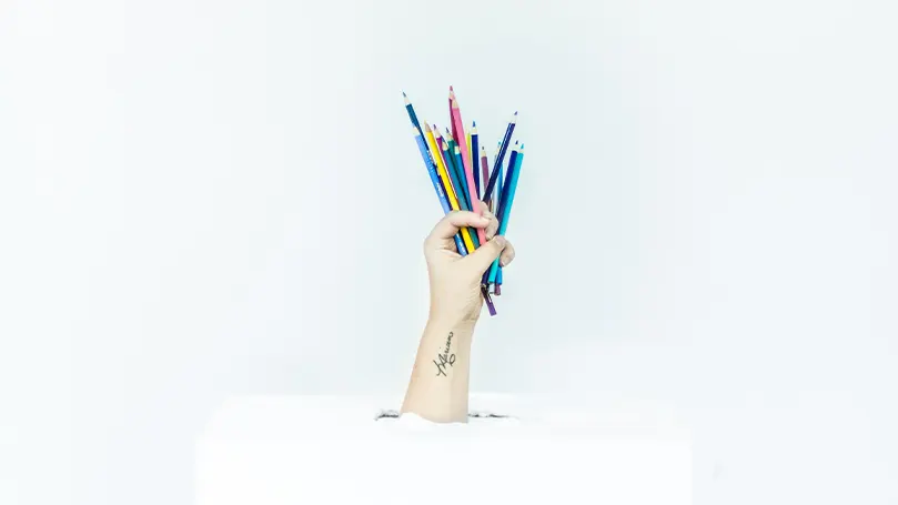 Une image d'une main tenant plusieurs crayons de couleur différents