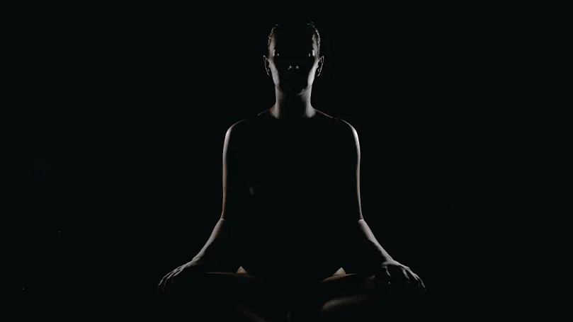 Image d'une personne méditant dans une pièce sombre.