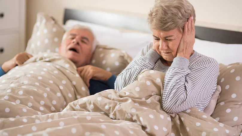 Image d'un vieux couple dans un lit où le mari ronfle et empêche sa femme de dormir.