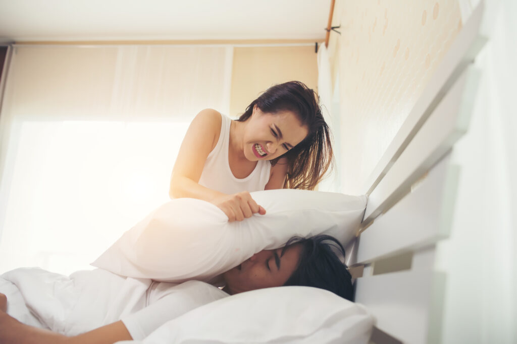 Image d'une femme plaçant un oreiller sur la bouche de son mari pour l'empêcher de ronfler.