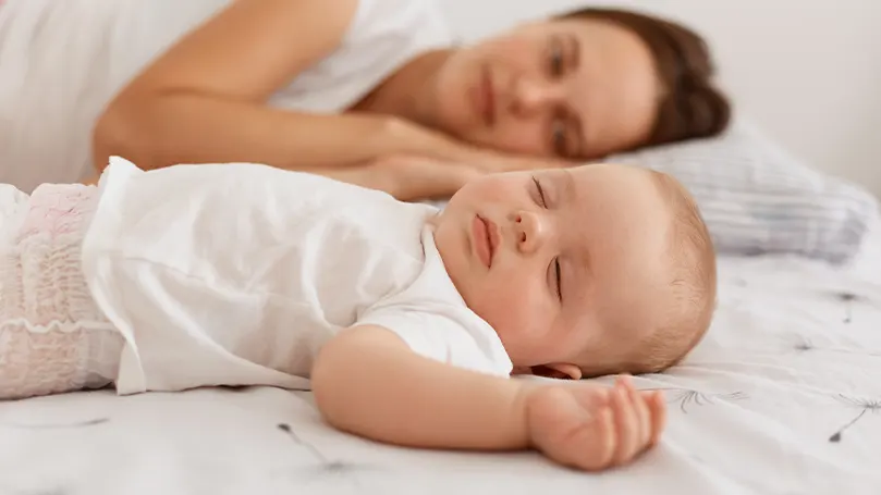 Image d'un bébé dormant à côté de sa mère.
