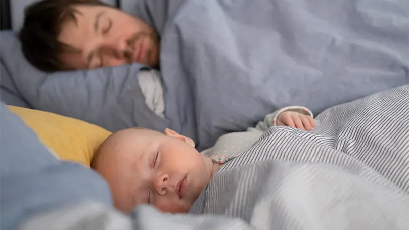 Image d'un bébé dormant à côté de son père.