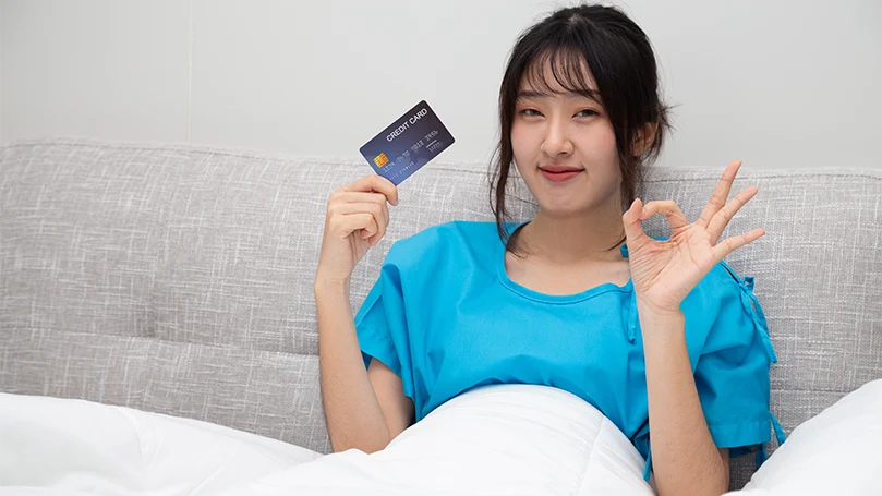Une femme asiatique au lit tenant sa carte de crédit