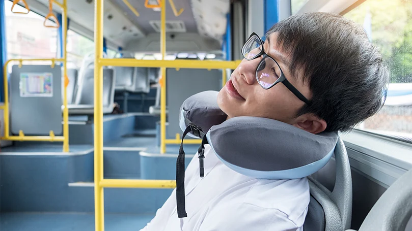Un homme dort avec un oreiller cervical dans un bus