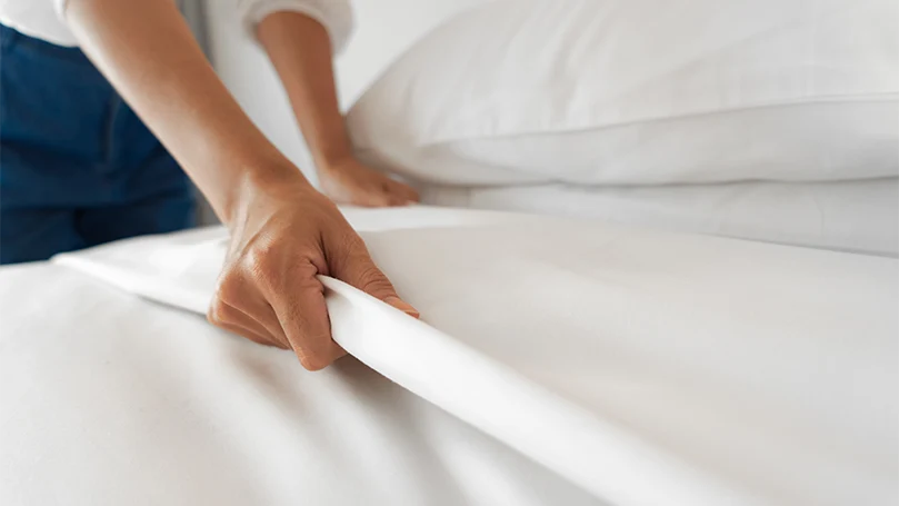 Image d'une femme installant un drap sur un lit.