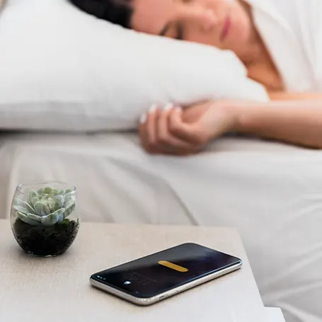 Une image d'une femme dormant avec son téléphone sur la table de nuit