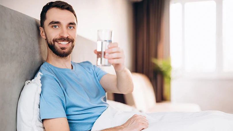 Image d'un homme buvant un verre d'eau dans son lit avant l'heure du coucher.