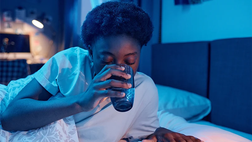 Image d'une femme buvant un verre d'eau avant de se coucher.