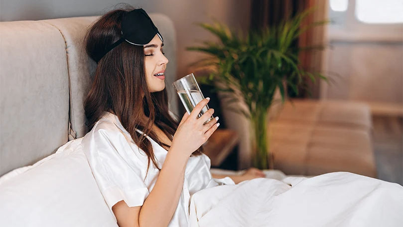 Image d'une jeune femme qui boit de l'eau avant de s'endormir.