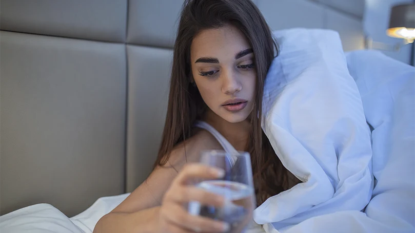 Image d'une jeune femme prenant un verre d'eau au lit.