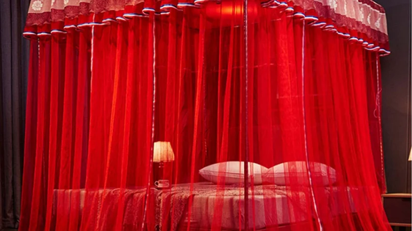 Image d'un luxueux lit à baldaquin entouré de riches draperies rouges.