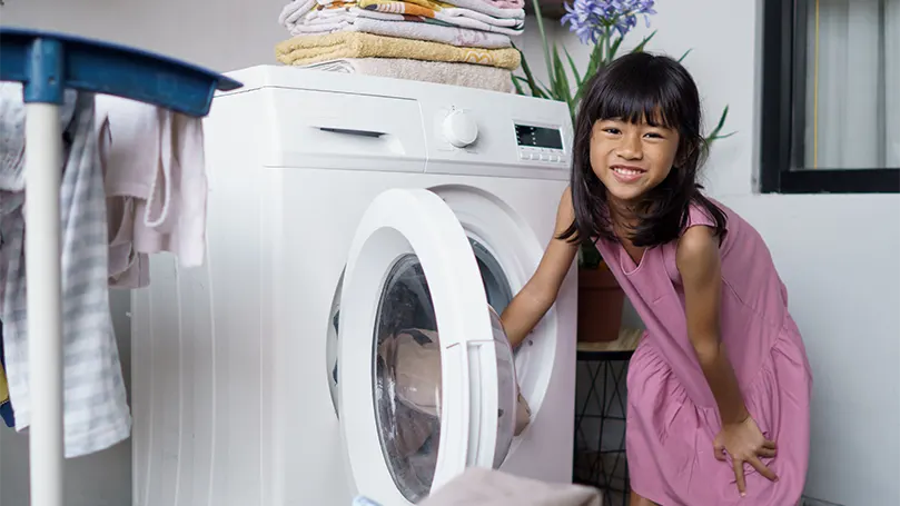 Image d'une petite fille mettant une couverture dans une machine à laver.