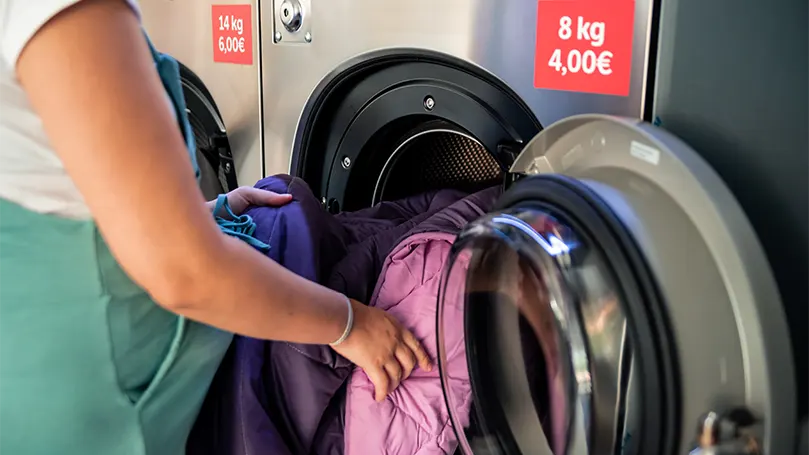 Image d'une femme enceinte mettant des couvertures dans une machine à laver.
