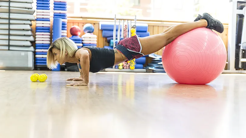 Une image d'une femme faisant des pompes inclinées sur un ballon de yoga.