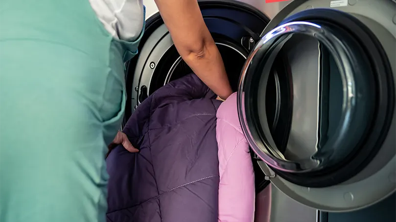 Image d'une femme mettant une couverture lestée dans une machine à laver.