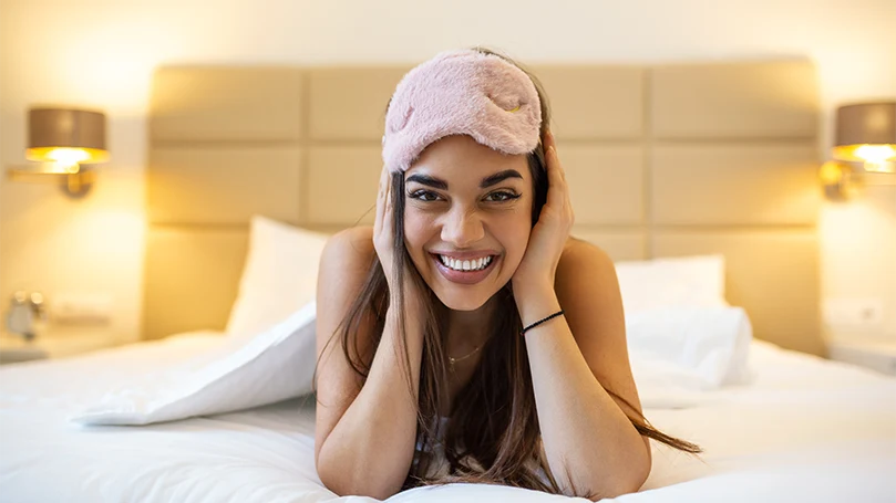 Image d'une jeune femme sur un lit avec un masque pour les yeux.