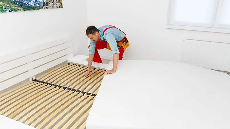 Image d'un jeune homme essayant de déterminer la raison du grincement de son lit.
