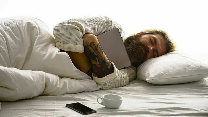 Image d'un homme barbu dormant profondément et étreignant une tablette.