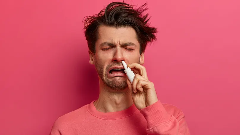 Image d'un homme souffrant d'allergies et utilisant des gouttes nasales.