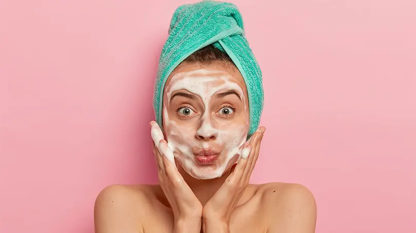 Image d'une femme mettant sur son visage un nettoyant pour le visage.