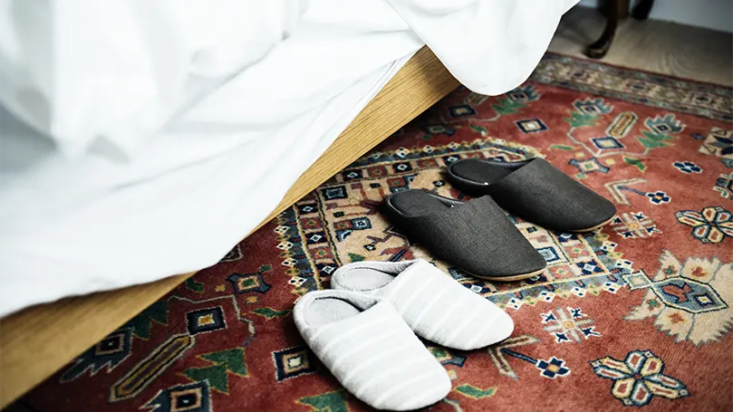 Image d'un tapis persan à côté d'un lit sur lequel sont posées deux paires de pantoufles.