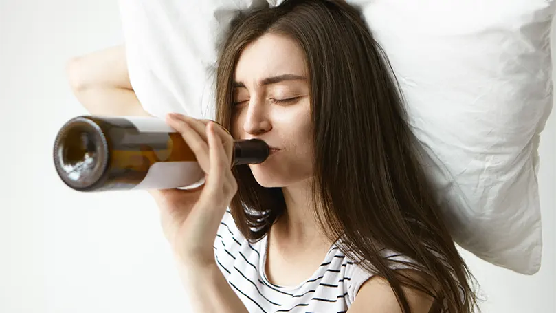 Image d'une femme buvant de l'alcool au lit.