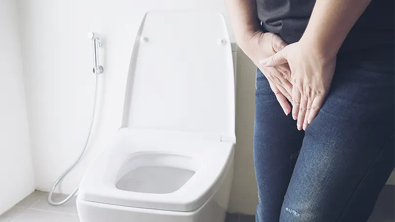 Image d'une femme se tenant la vessie en raison d'un besoin d'uriner à côté des toilettes.