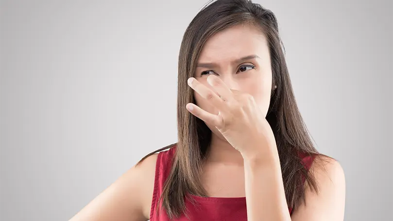 Image d'une femme se tenant le nez à cause d'une odeur désagréable de moisi.