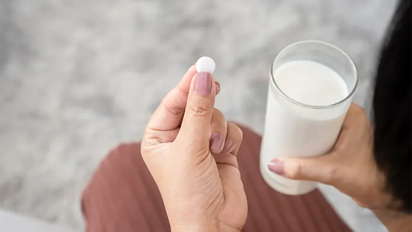Une femme prenant une pilule de mélatonine avec un verre de lait.