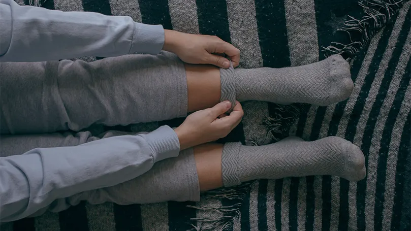 Image d'une femme mettant ses chaussettes au lit.