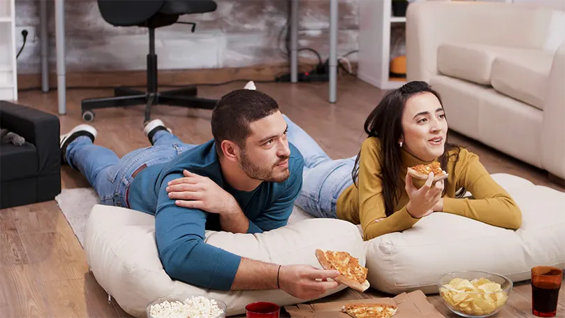 Image d'un couple sur le sol en train de manger une pizza.