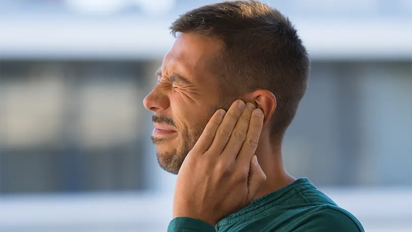 Un homme souffrant d'une rupture du tympan se tient l'oreille à cause de la douleur.