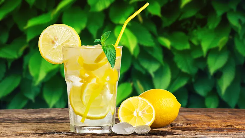 un verre d'eau citronnée à côté de deux citrons sur une table.