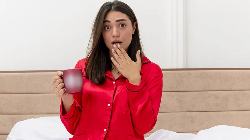 Image d'une femme en pyjama rouge qui boit de l'eau parce qu'elle s'est réveillée la bouche sèche.