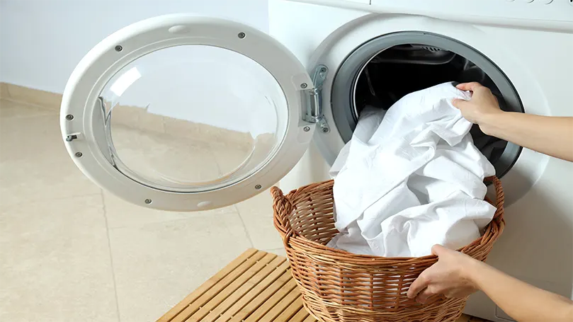 une femme qui met des draps blancs dans une machine à laver.