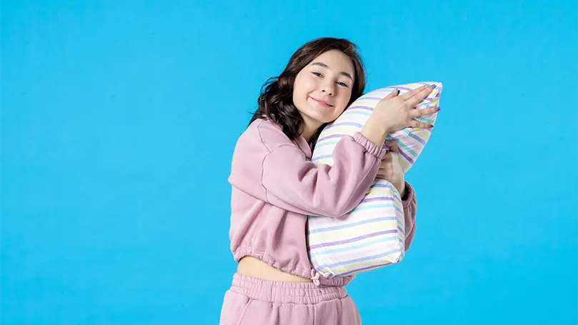 Image d'une jeune femme serrant un oreiller avec ses mains.