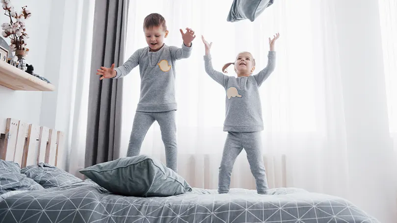 Image de deux jeunes enfants sautant sur le lit.