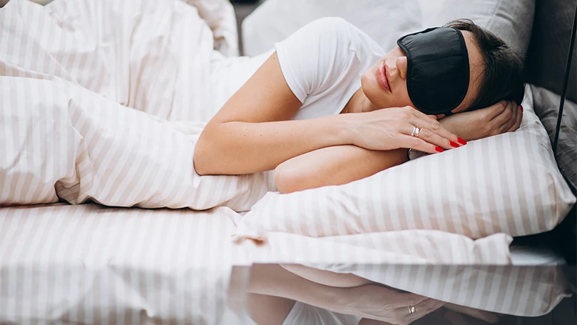 Image d'une femme avec un masque de sommeil dormant dans un lit.