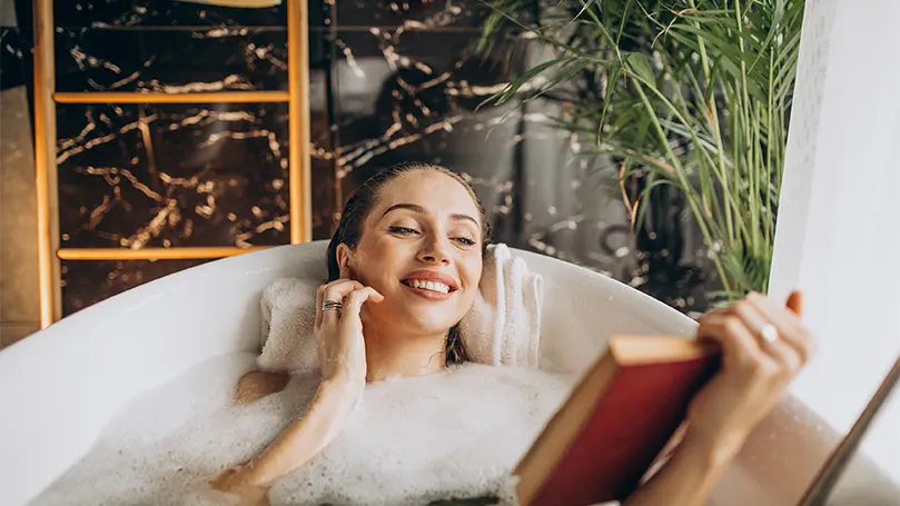 Image d'une femme confortablement allongée dans une baignoire remplie, lisant un livre et s'amusant.