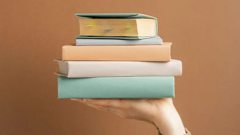 Image d'une main tenant des livres empilés.