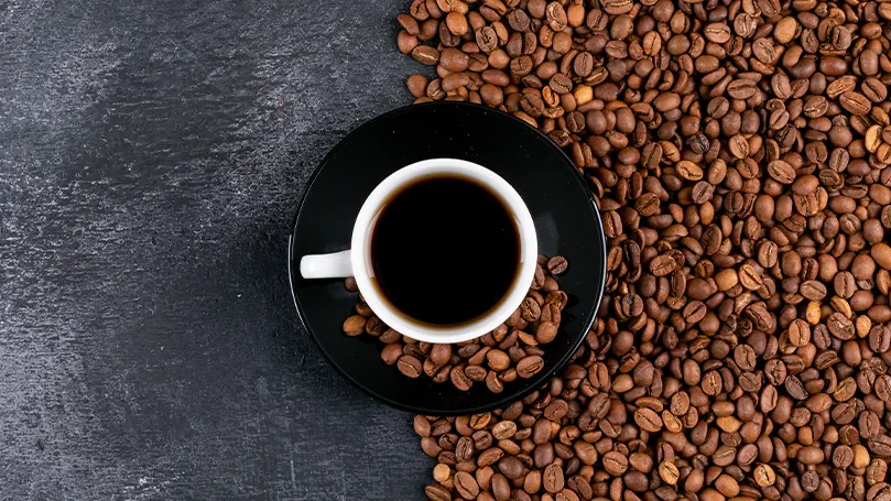 Image d'une tasse de café entourée de grains de café