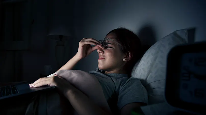 Image d'une femme au lit la nuit, se tenant le visage en signe de douleur.