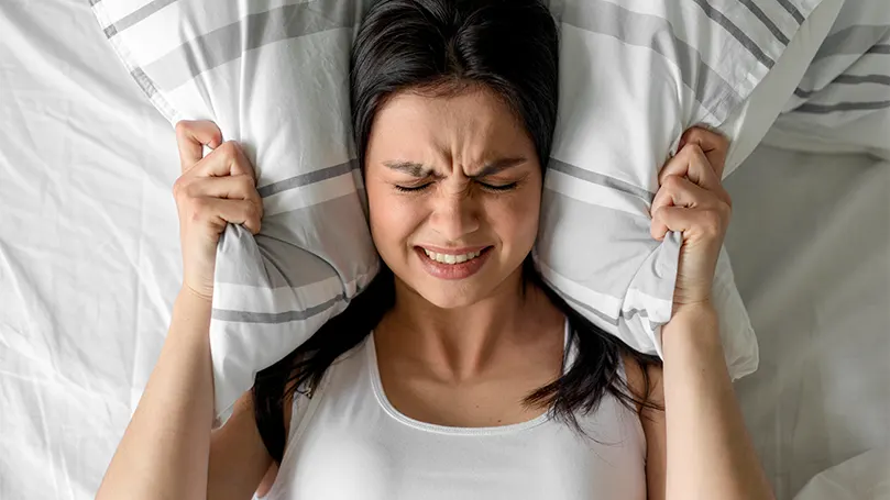 Image d'une femme se couvrant les oreilles avec son oreiller
