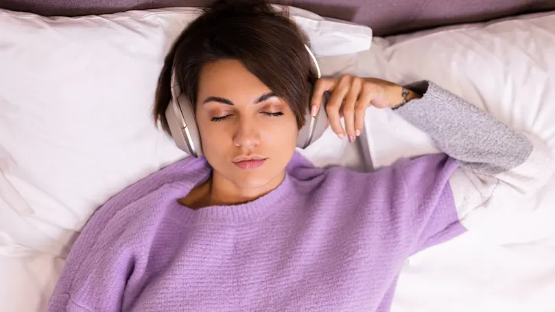 Image d'une femme au lit avec des écouteurs.