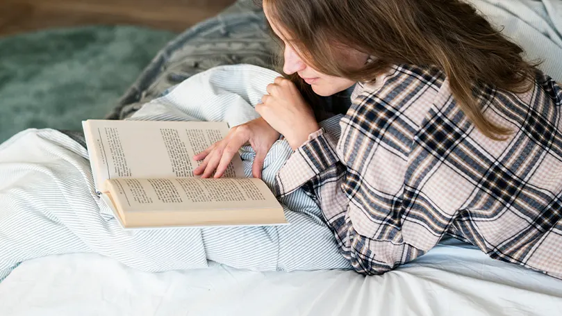 Image d'une femme lisant un livre au lit.