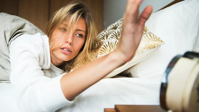 Image d'une femme qui attrape son réveil alors qu'elle est au lit.