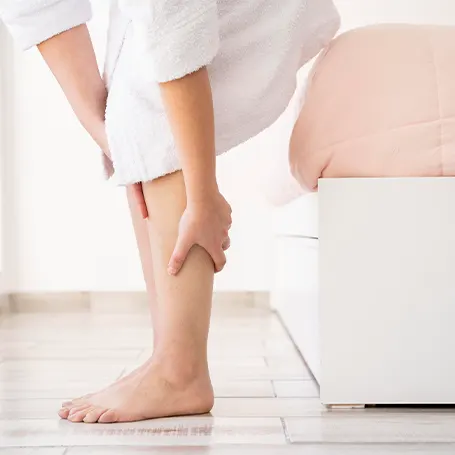Image d'une femme assise sur son lit et se tenant la jambe en raison de la douleur.