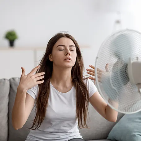 Image d'une femme qui se rafraîchit en pointant un ventilateur sur elle.