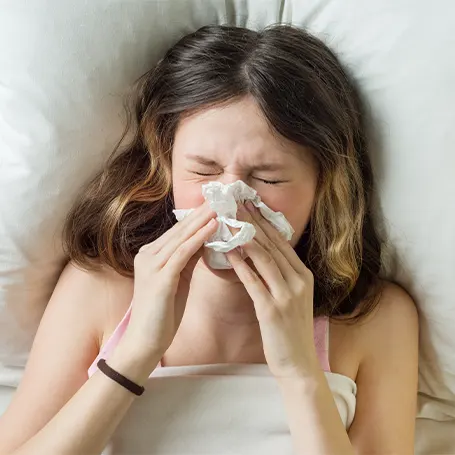 Image d'une femme portant un mouchoir à son nez après que sa literie a déclenché ses allergies.