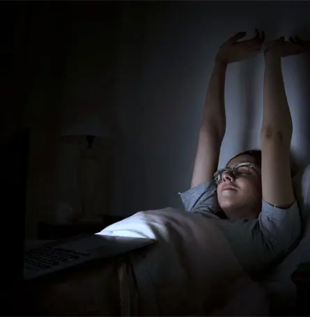 Image d'une femme au lit, dont le visage est éclairé par une lumière artificielle.